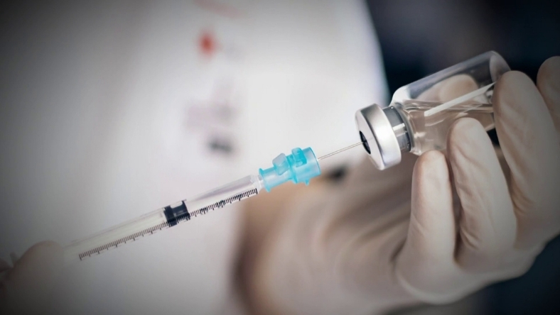 Medical professional preparing vaccine dose from vial using syringe in clinical setting