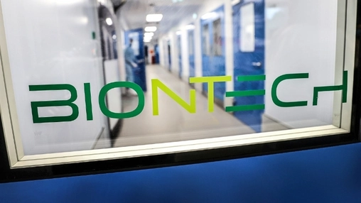 BioNTech logo on a glass partition overlooking a pharmaceutical cleanroom corridor with blue-framed doors