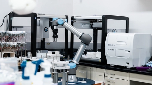 Laboratory robotic arm between two Opentrons workstations with sample tubes and a BioTek reader nearby