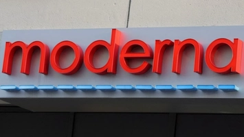 Close-up of Moderna red logo letters on a grey building facade with a row of blue rectangular tiles beneath